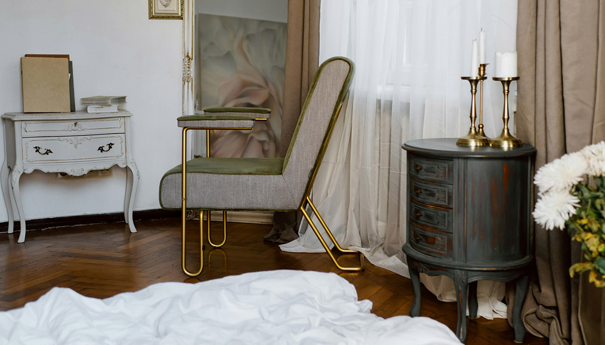 Angolo lettura in stile vintage con poltrona retr&ograve;, comodino d&rsquo;epoca e tende chiare