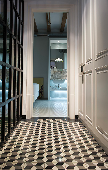 Corridoio con pavimento a mosaico geometrico in bianco e nero e vista su bagno luminoso con vasca freestanding.