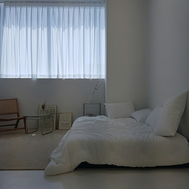 Camera minimal con letto basso, arredi essenziali e luce filtrata da tende chiare.