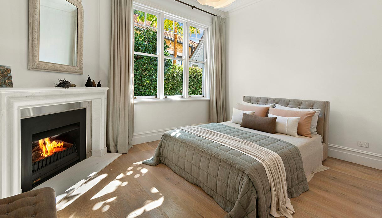 Camera da letto luminosa con camino classico in marmo, letto matrimoniale e arredi neutri.