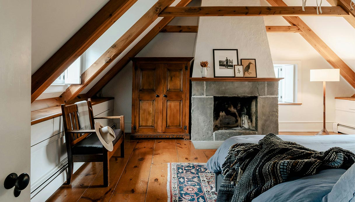 Camera da letto in mansarda con camino in pietra, travi in legno a vista e arredi rustici.