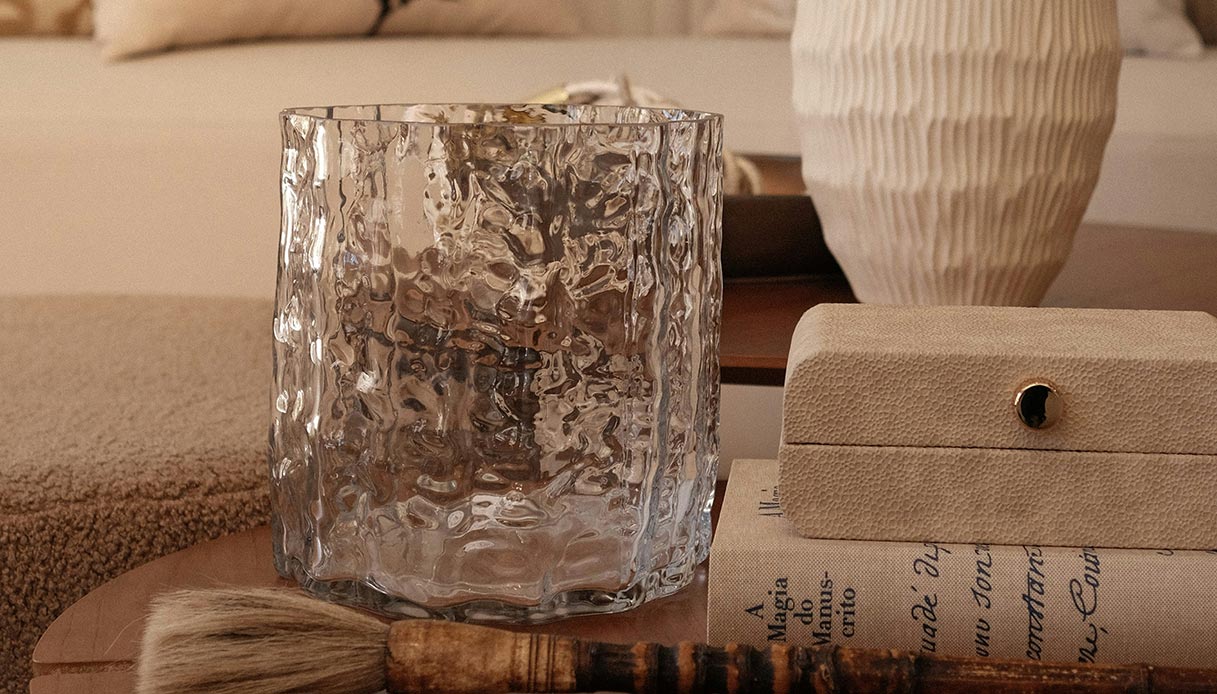 Vaso in vetro trasparente testurizzato su tavolino in legno con oggetti decorativi neutri