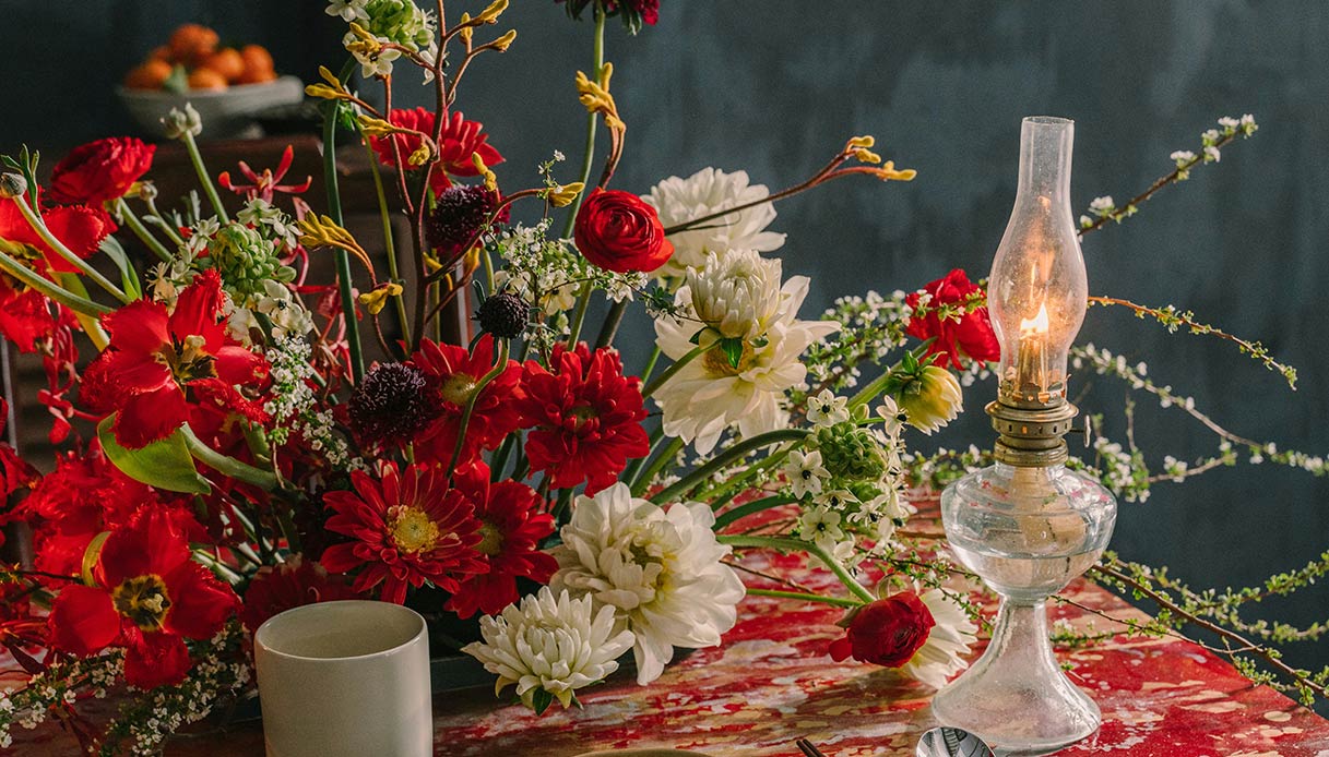 Centrotavola invernale con fiori rossi, candele e luce calda su tavola apparecchiata