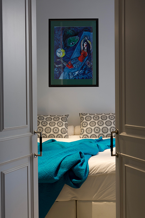 Camera da letto con coperta azzurra, cuscini decorativi e quadro appeso sopra il letto.