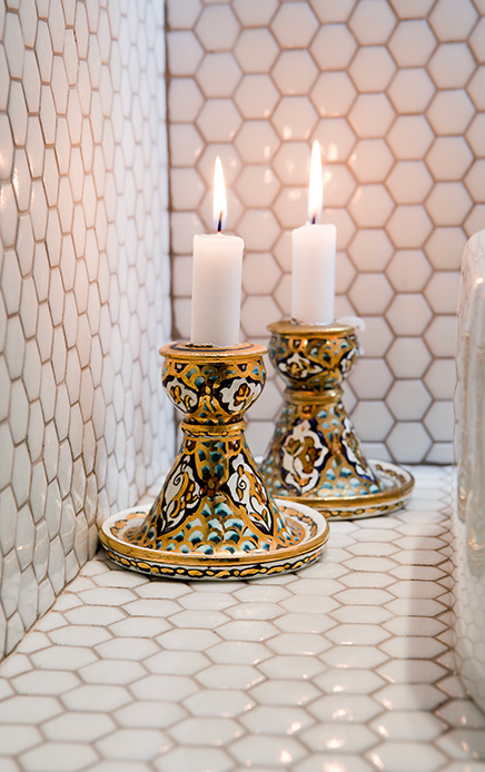 Dettaglio di due candelieri in ceramica decorata con candele accese su piastrelle esagonali.
