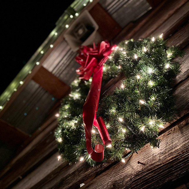 Grande ghirlanda verde con luci bianche e fiocco rosso appesa a una parete esterna