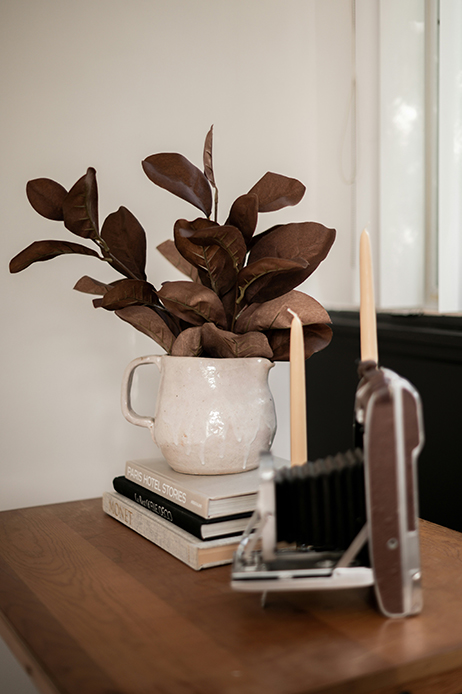 Brocca in ceramica chiara con foglie decorative scure su tavolo in legno