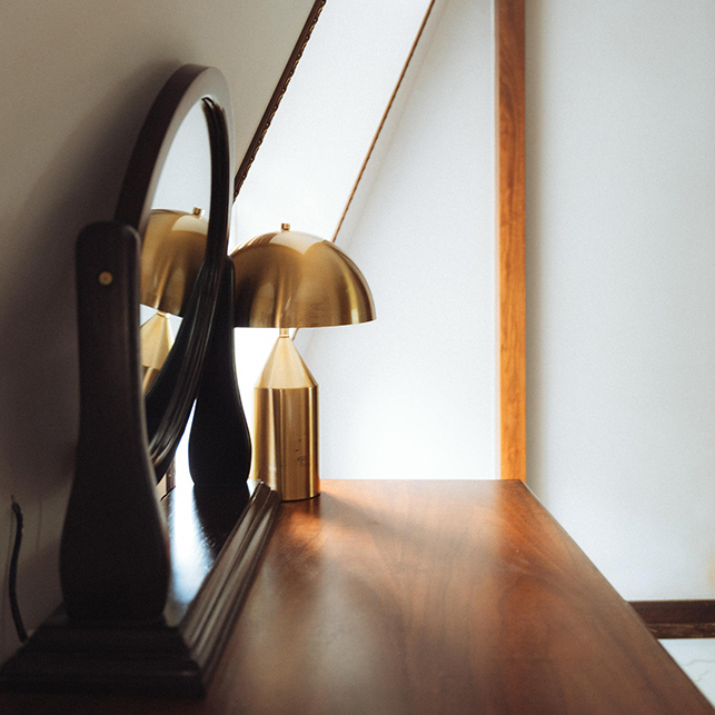 Lampada in ottone riflessa in uno specchio su un mobile in legno in stile minimalismo caldo