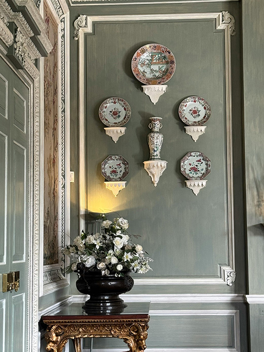 Parete in stile castlecore con piatti decorativi antichi, cornici classiche e consolle in legno intagliato.