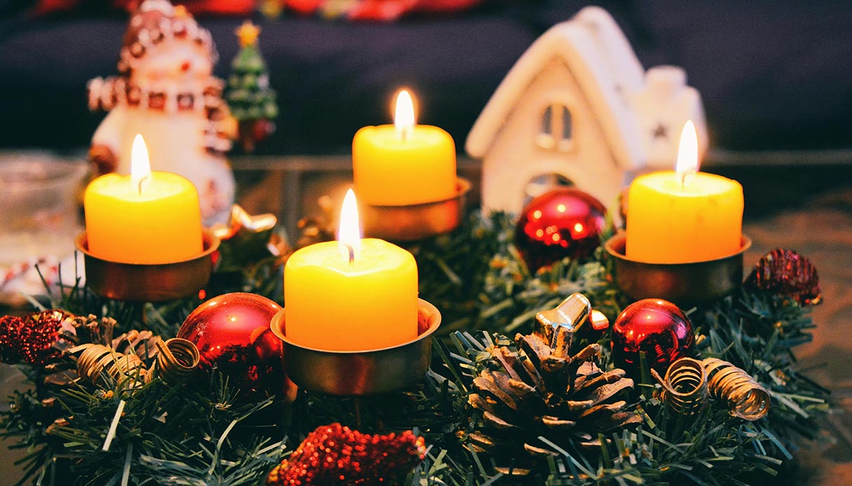 Centrotavola natalizio con candele gialle e decorazioni rosse e verdi.