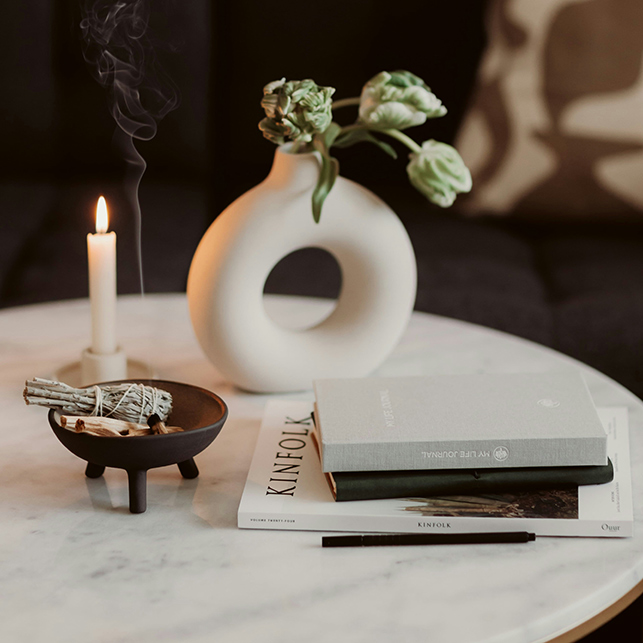 Tavolino rotondo con candela accesa, vaso scultoreo e libri