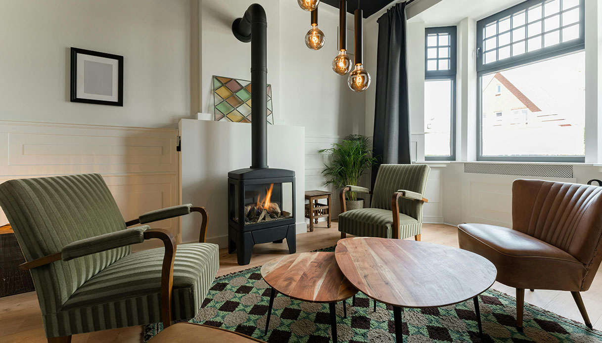 Salotto in stile vintage contemporaneo con poltrone anni &rsquo;50, tavolini in legno e stufa nera a vista