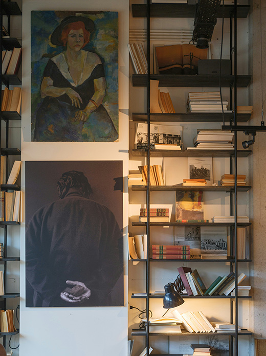 Parete con quadri figurativi appesi accanto a una libreria a giorno con libri e oggetti decorativi.