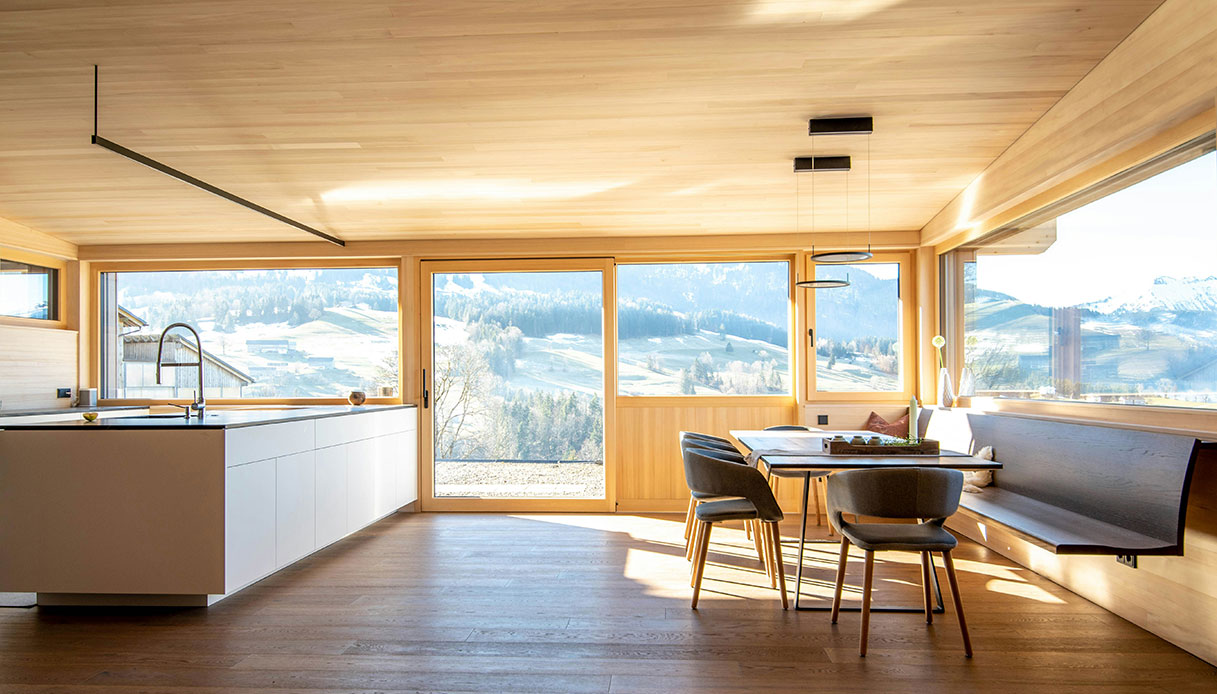 Soggiorno di montagna con arredi in legno e ampie finestre sulla natura.