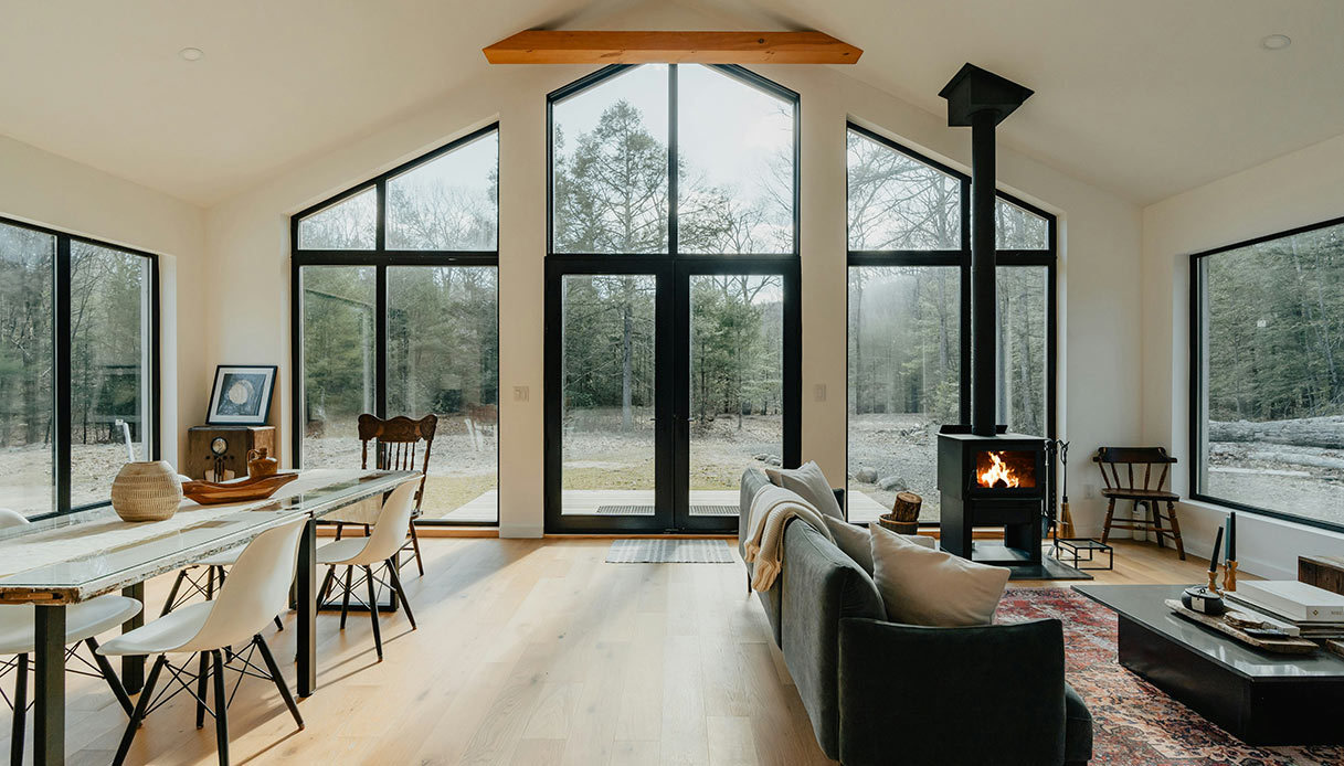 Interno di chalet contemporaneo con grandi vetrate e caminetto acceso.