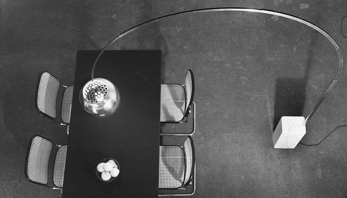 Arco dei Castiglioni fotografata dall&rsquo;alto mentre illumina un tavolo rettangolare con sedie