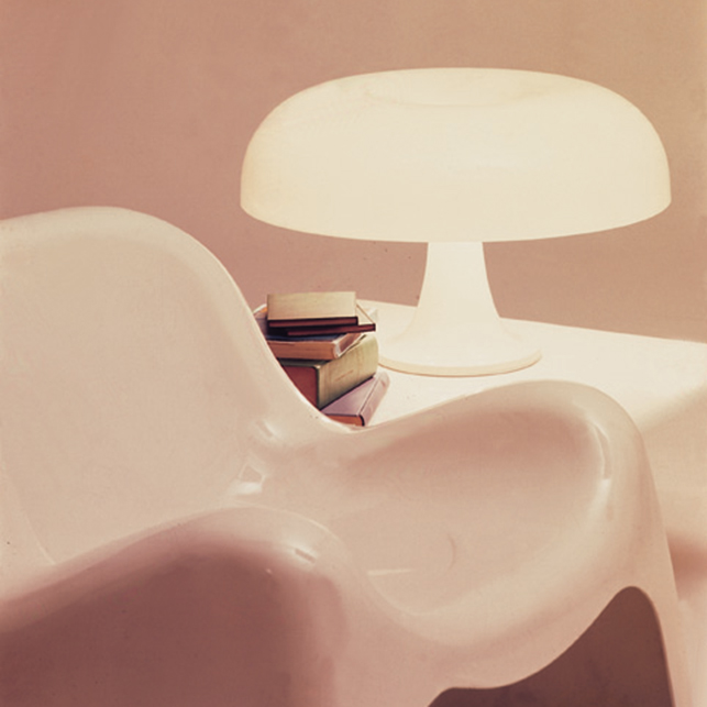 Lampada Nesso bianca accesa su un tavolino accanto a una poltrona moderna