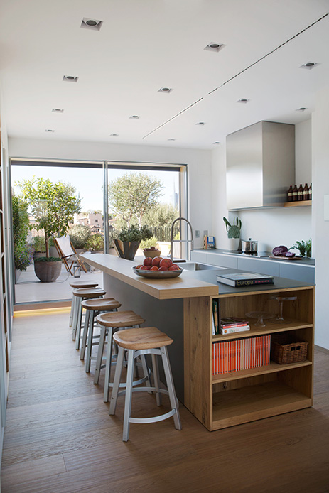 Cucina open space con isola in legno, sgabelli in massello e vetrate a tutta altezza con accesso alla terrazza