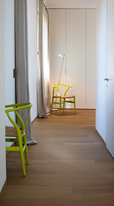 Disimpegno luminoso con sedia Wishbone verde, parquet in rovere e armadiature bianche a filo muro