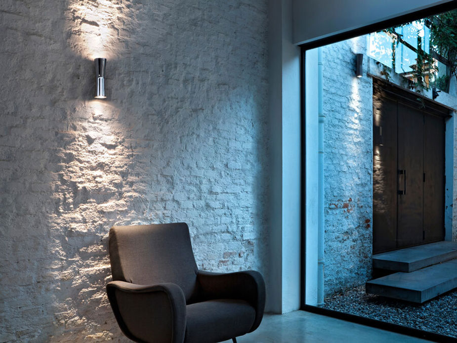 Applique cromata Clessidra di Flos design Antonio Citterio con luce diretta e indiretta su parete materica