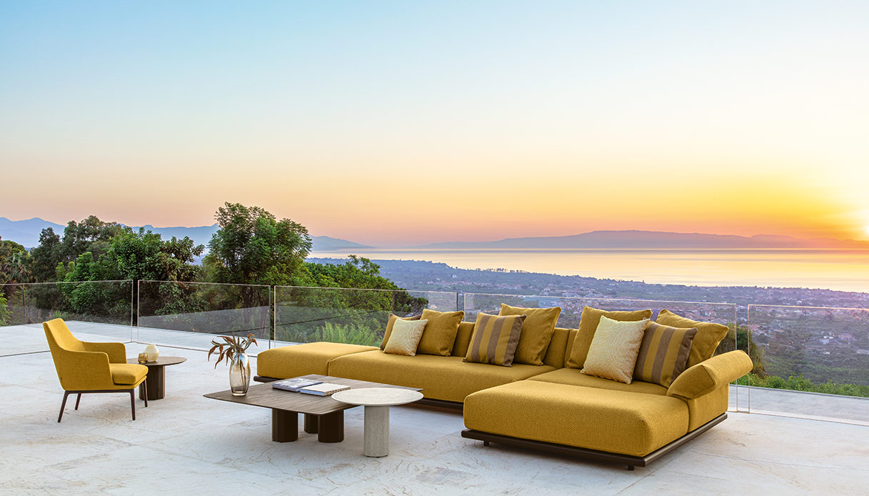 Divano outdoor Elton color ocra con tavolini rotondi su terrazza vista mare al tramonto