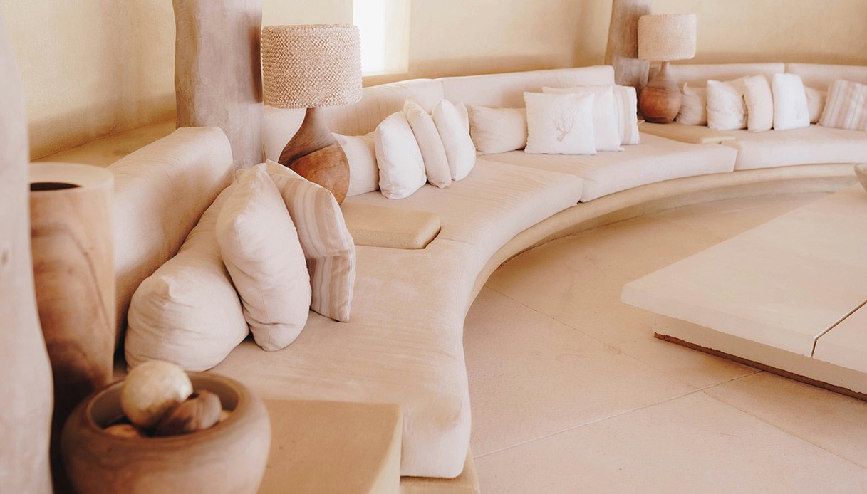 Salotto ribassato curvo con divani beige e cuscini chiari in ambiente minimal dalle tonalit&agrave; calde