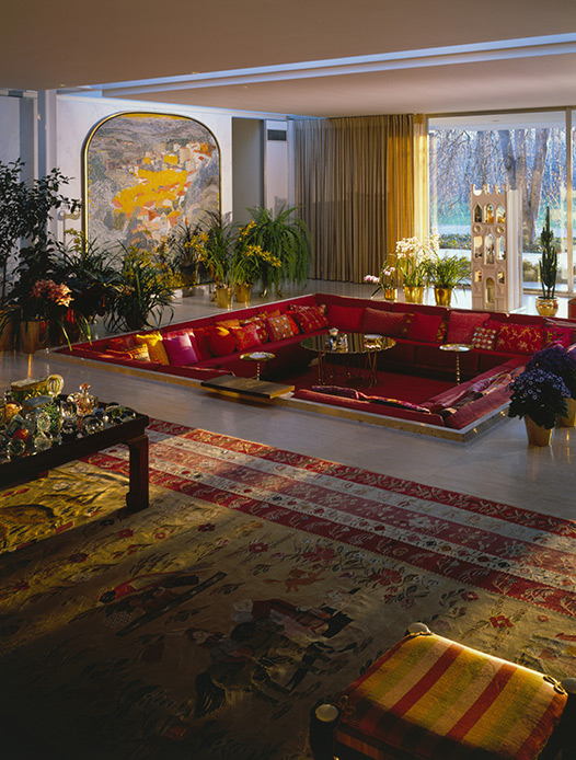 Living anni Settanta con salotto ribassato rosso, tappeto orientale e grandi vetrate affacciate sul parco