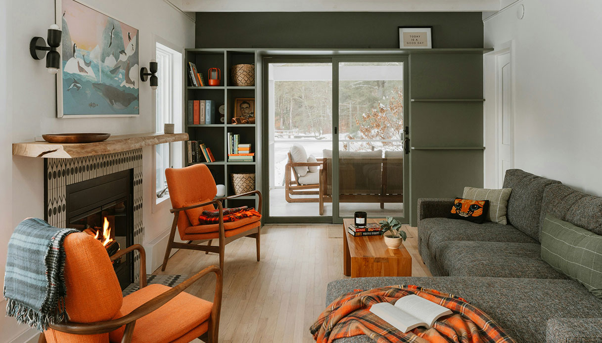 Living con parete verde salvia, camino acceso e poltrone arancioni in stile moderno