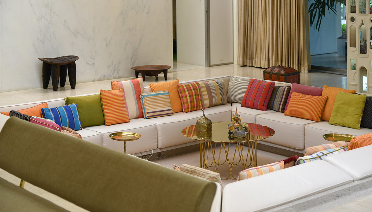 Salotto ribassato moderno con divani bianchi disposti a U e cuscini multicolor attorno a tavolino centrale in metallo