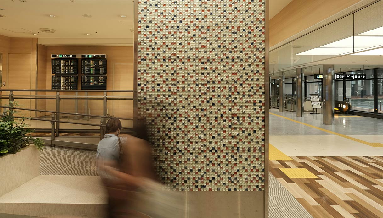 Parete rivestita in mosaico con piccole tessere nei toni del rosso, bianco e blu in un ambiente pubblico con pavimento in legno