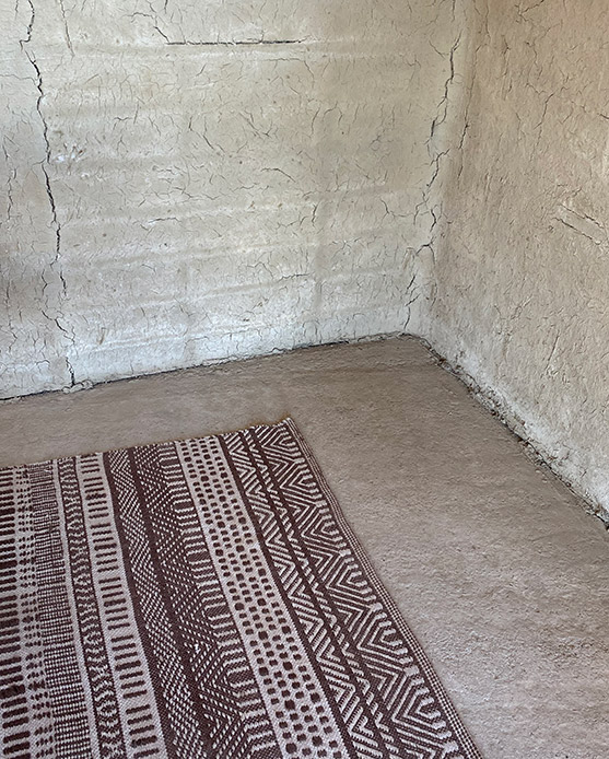 Parete interna con finitura in terra naturale e tappeto tessile dai motivi geometrici