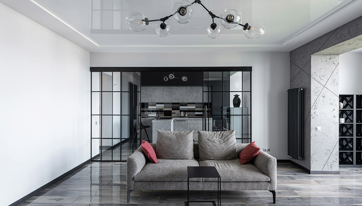 Open space in stile quiet luxury con divano grigio, pareti in vetro e finiture in pietra