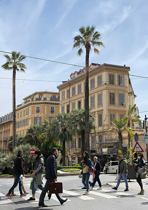 Palazzi in stile Liberty a Sanremo con palme e persone che attraversano la strada