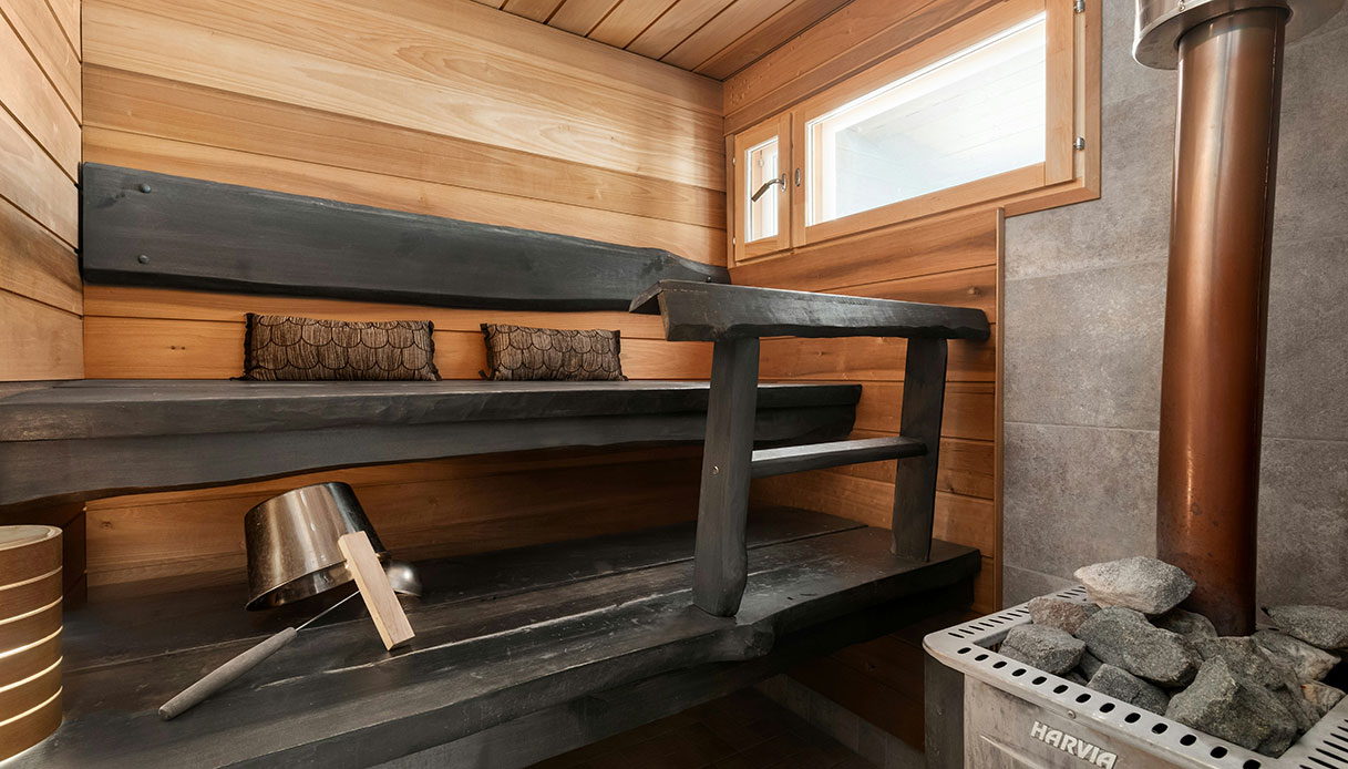 Sauna interna in legno con panche scure e stufa a pietre