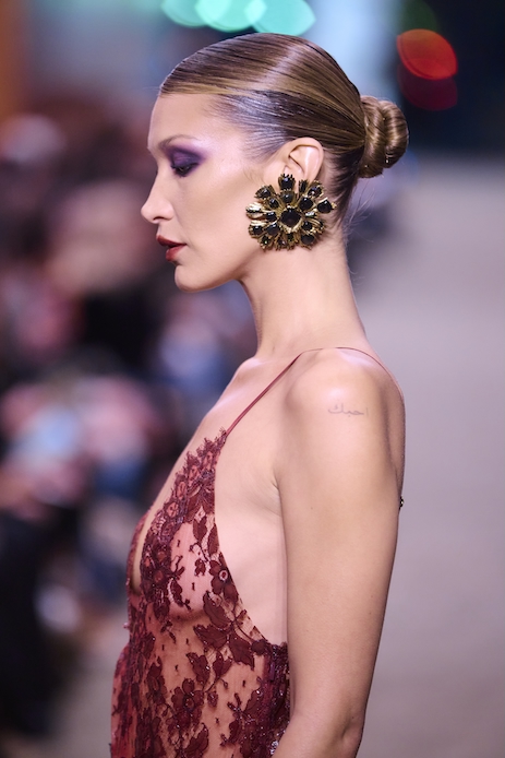 Bella Hadid sfila alla Paris Fashion Week 2026 con body in pizzo rosso e gonna trasparente nera