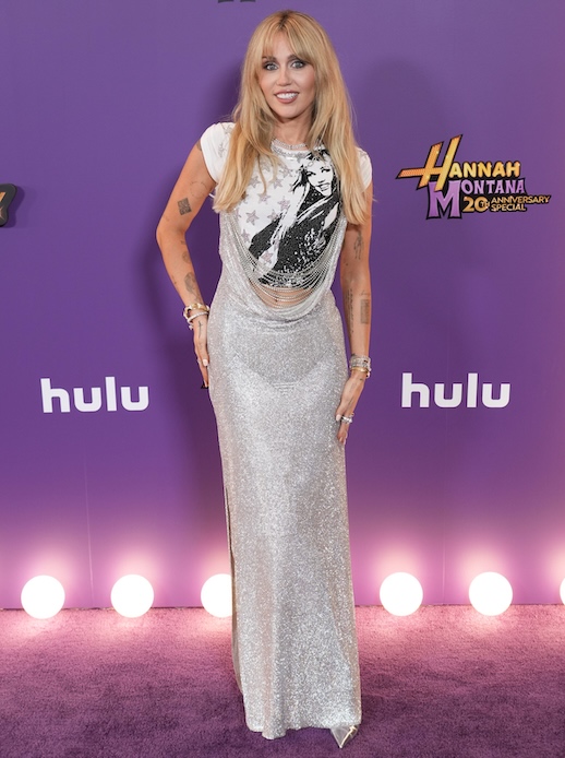 Miley Cyrus sul red carpet Hannah Montana anniversary con abito lungo silver e T-shirt grafica