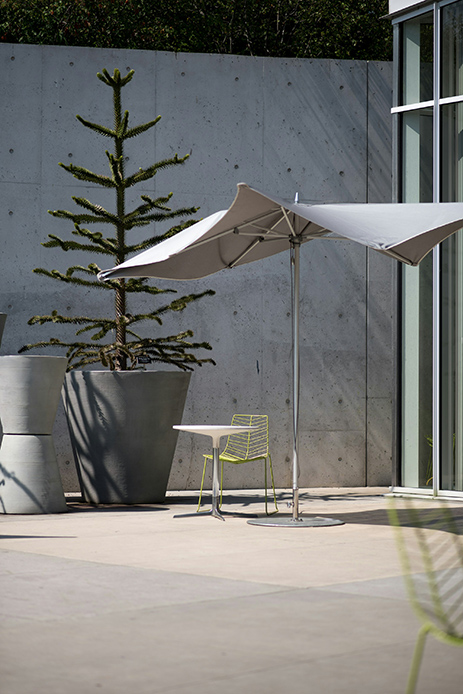 Ombrellone chiaro su terrazza contemporanea con pavimento in cemento e grandi vasi decorativi