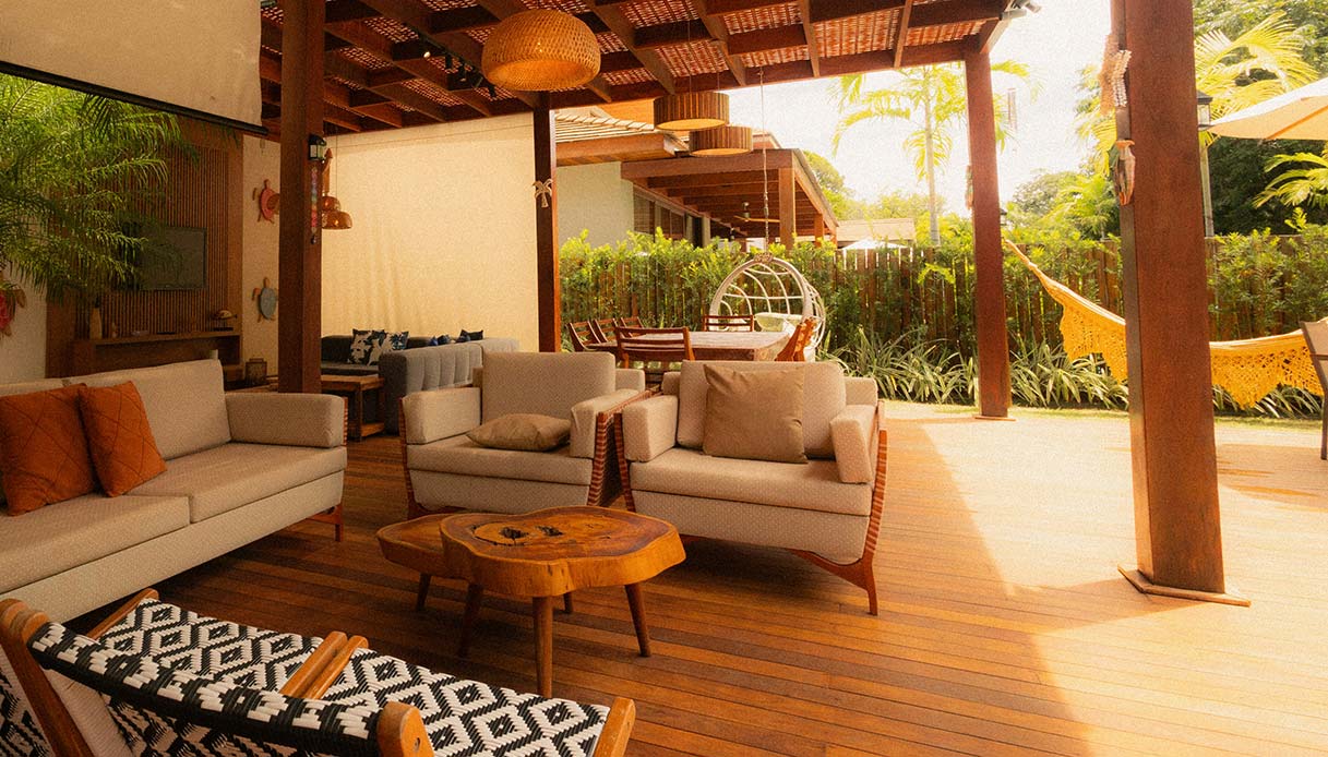 Pergola in legno che copre un salotto da esterno con divani chiari e tavolino su pavimento in legno