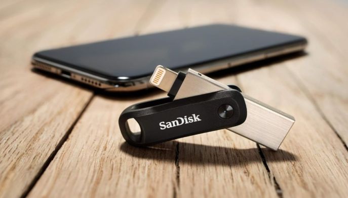 Chiavetta SanDisk iXpand con connettore Lightning aperto, appoggiata su una superficie in legno accanto a uno smartphone iPhone