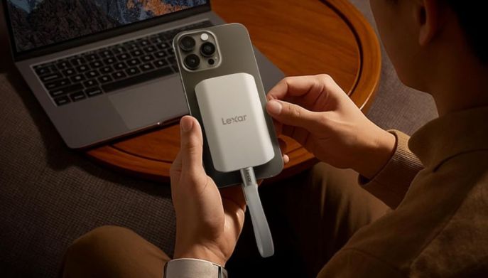 Mani che collegano un mini SSD portatile Lexar ES5 al dorso di un iPhone, con un MacBook sullo sfondo