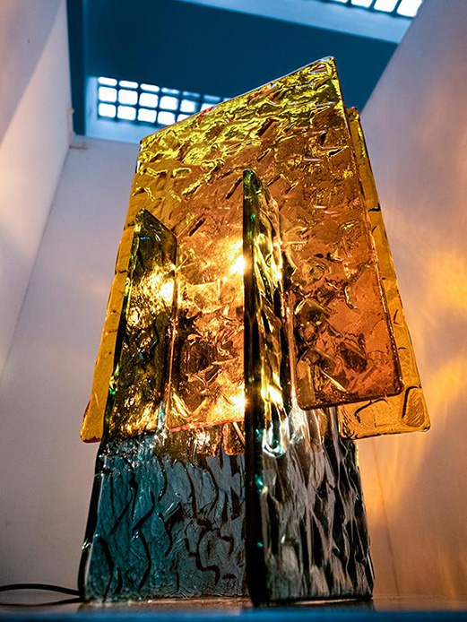 Scultura luminosa in vetro colorato del duo 6:AM alla Piscina Romano, lastre irregolari in giallo arancio e verde-azzurro illuminate dall'interno