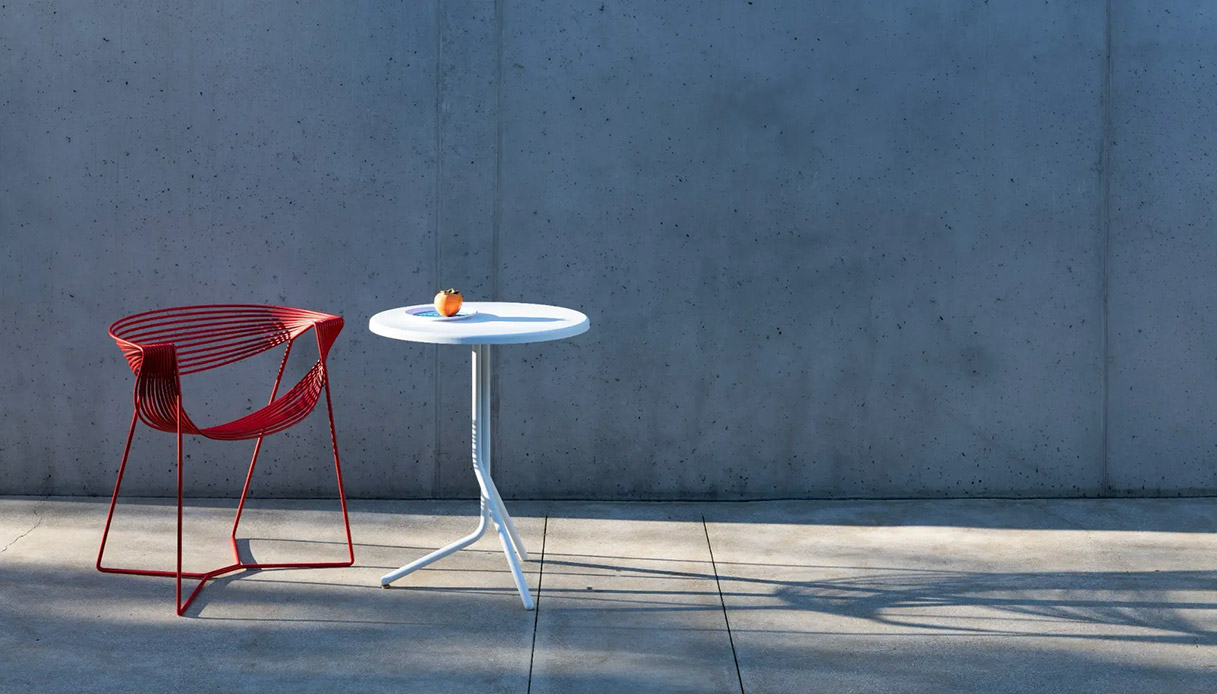 Sedia outdoor Filuferru di Robby Cantarutti in acciaio rosso con tavolino rotondo bianco su pavimento in cemento