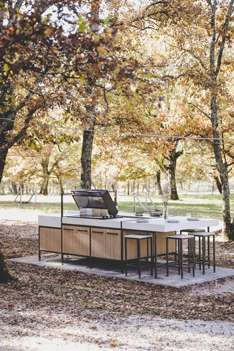Cucina outdoor a isola Otok di Evoluta con struttura in metallo scuro e piano in pietra chiara in un parco con alberi autunnali
