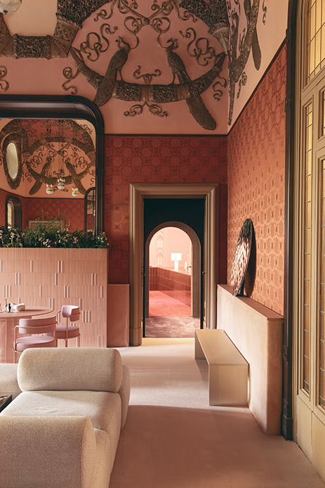 Interno con pareti rivestite di carta da parati rosa e rossa, soffitto affrescato, archi e arredi contemporanei.