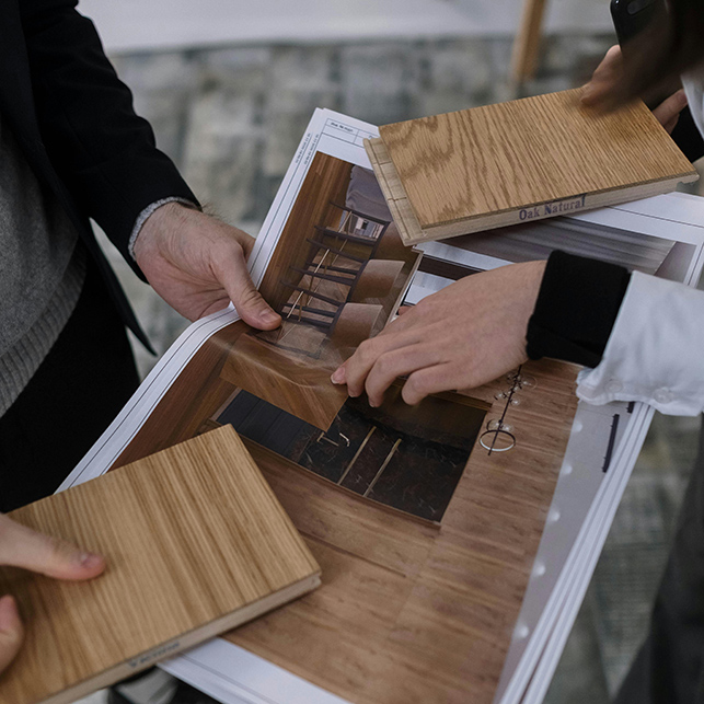 Mani che reggono campioni di parquet in rovere naturale sovrapposti a un progetto di interior design su carta