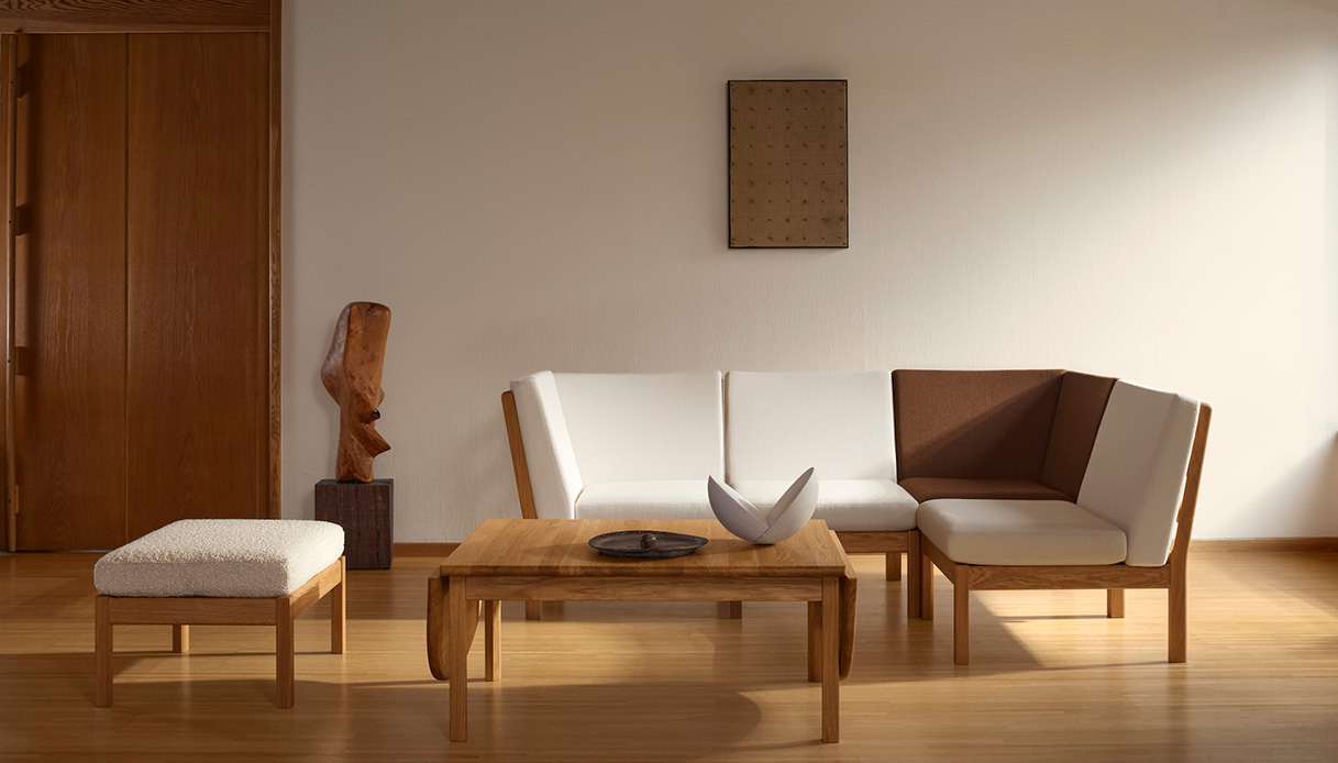 Living con divano modulare e poltrona in rovere oliato con tappezzeria bianca e marrone, tavolino in legno e scultura organica in legno su pavimento in parquet chiaro