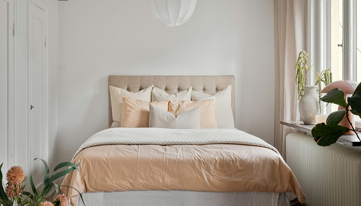 Camera da letto cocoon style con testiera imbottita beige e biancheria in tonalit&agrave; pesca e crema