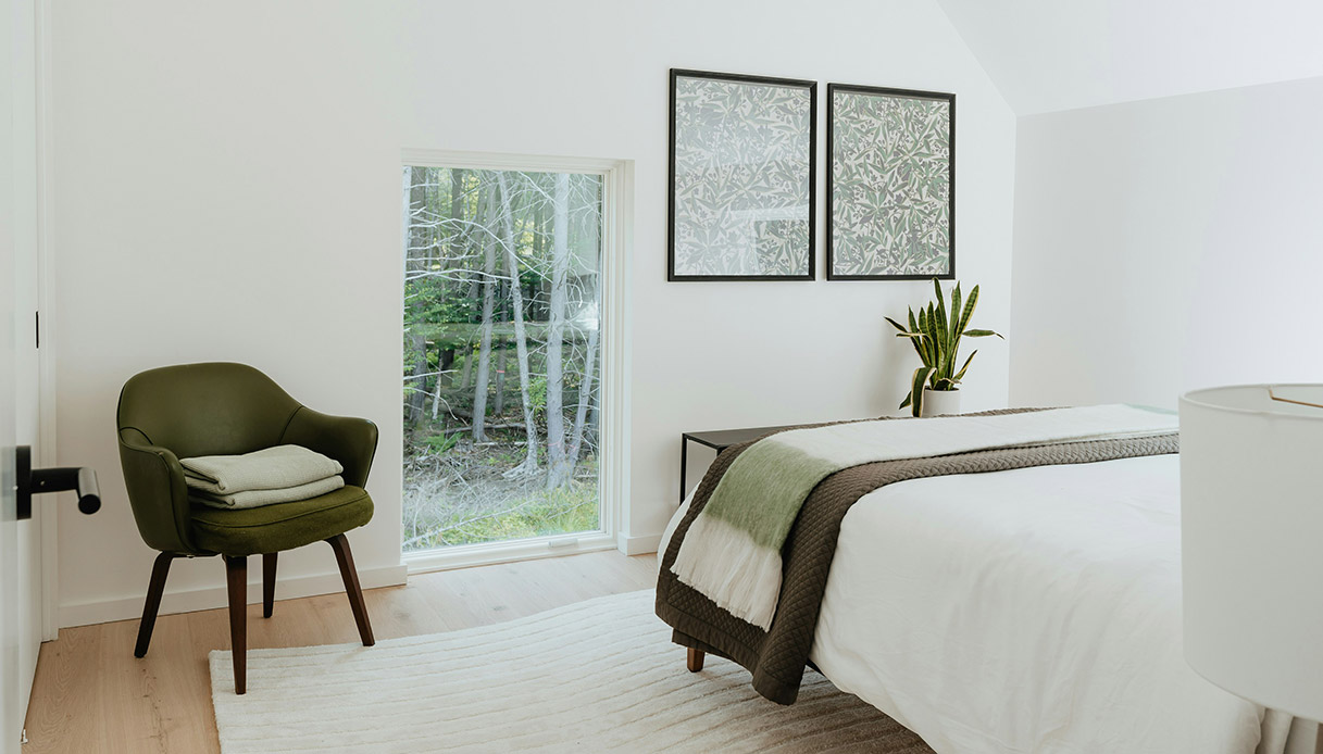 Camera da letto cocoon style con poltrona verde e finestra sul bosco