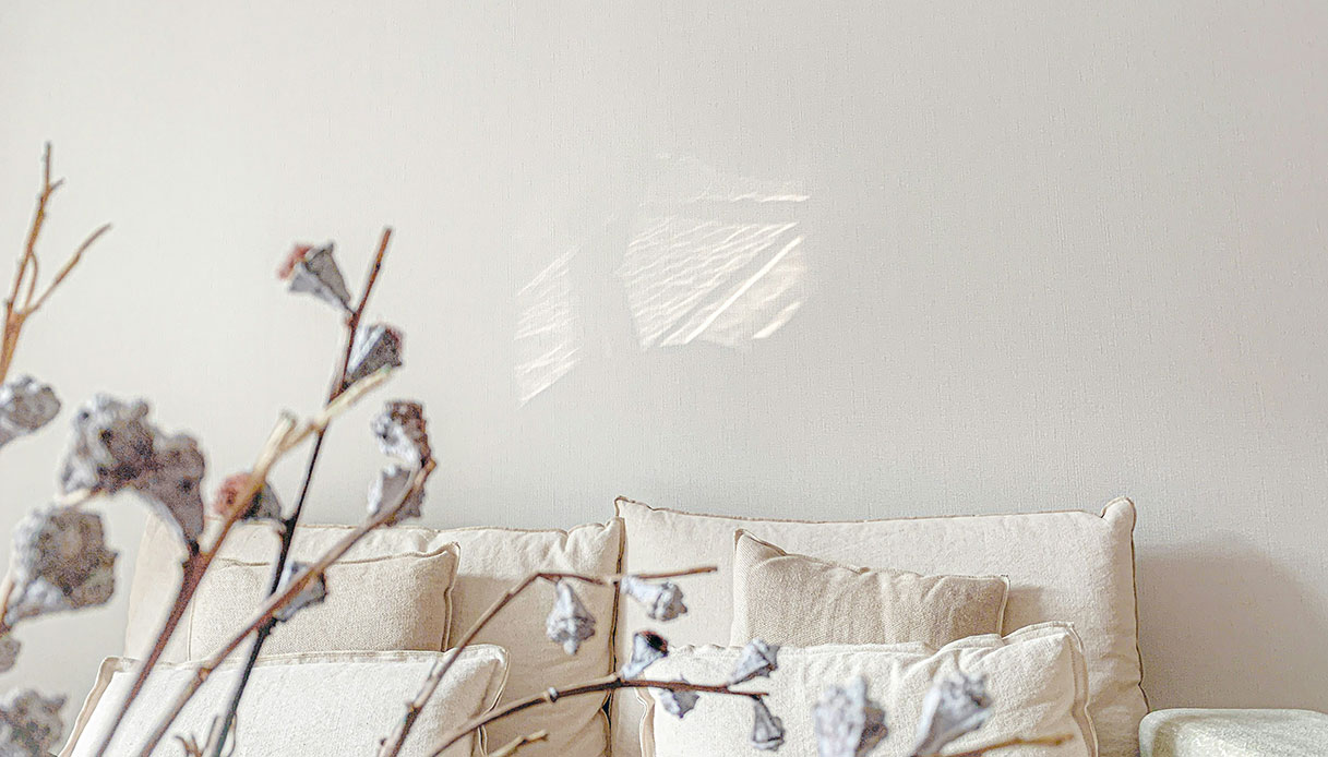 Divano con cuscini crema e rami secchi in un interno cocoon style con luce naturale