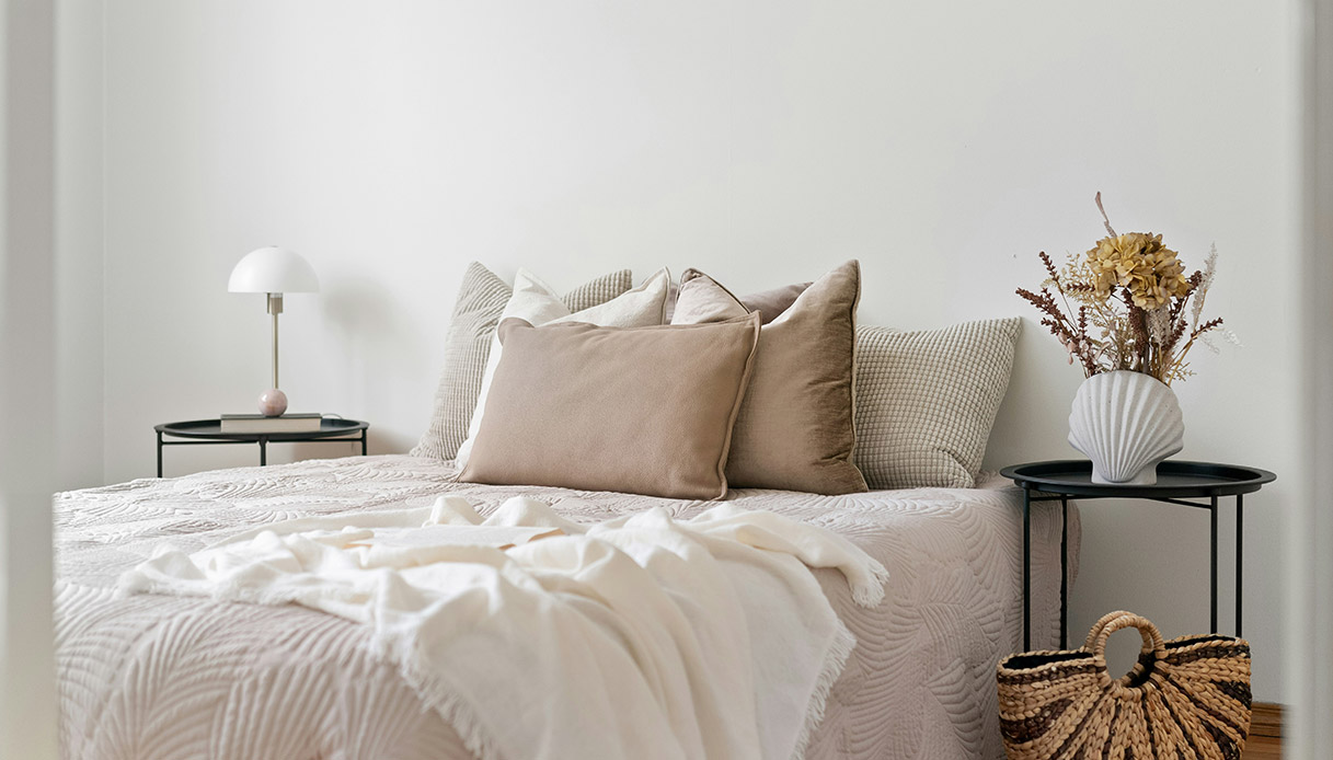 Letto con cuscini in toni sabbia e plaid bianco in stile cocoon